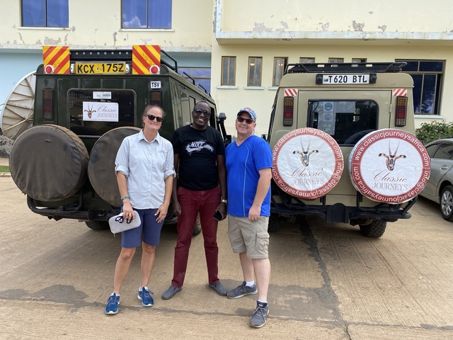       Three people standing by safari vehicles in parking area.
  