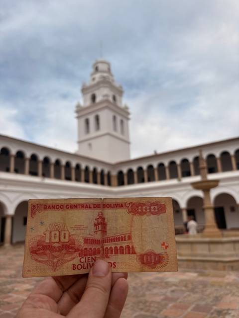 Hand holding Bolivian currency with a building in the background.