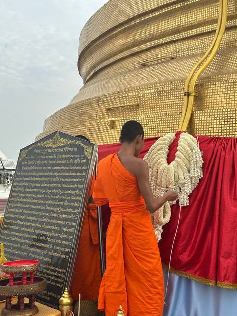       Monk in orange robe standing near temple architecture.
  