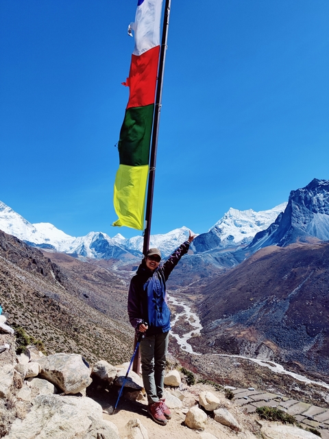 Person posing with a flag against a backdrop of snowy mountains.