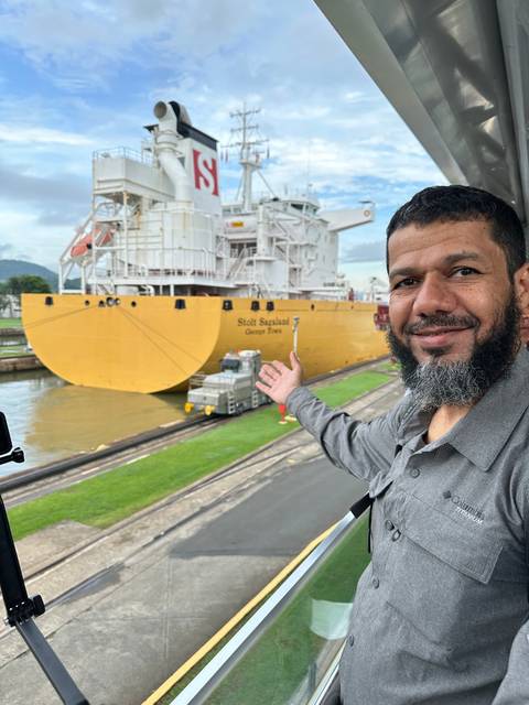       Man standing next to a canal with a large ship passing through.
  