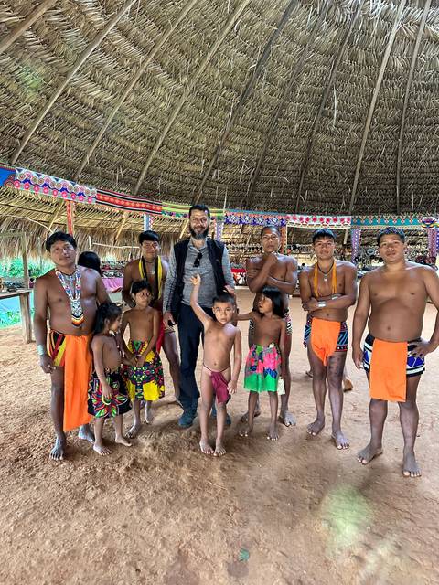       Group photo of people in traditional attire under a thatched roof.
  