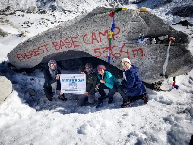 Group of people celebrating at the Everest Base Camp marked by a large rock.