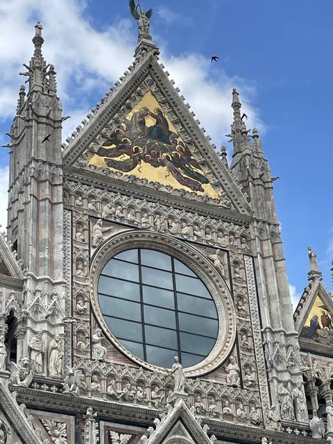       Facade of an ornate building with a golden mural and large round window.
  