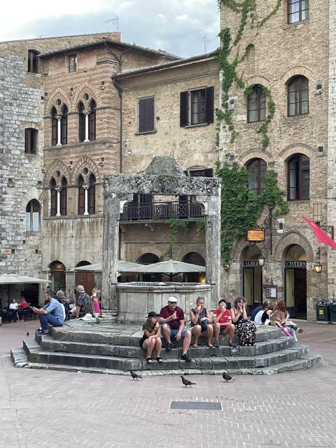       People sitting on steps around a historical fountain in a town square.
  