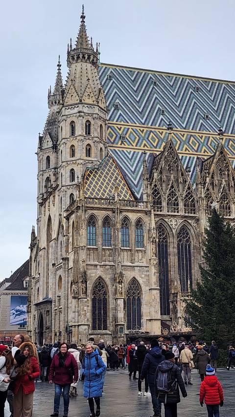 Colorful roofed cathedral in a public square bustling with tourists.