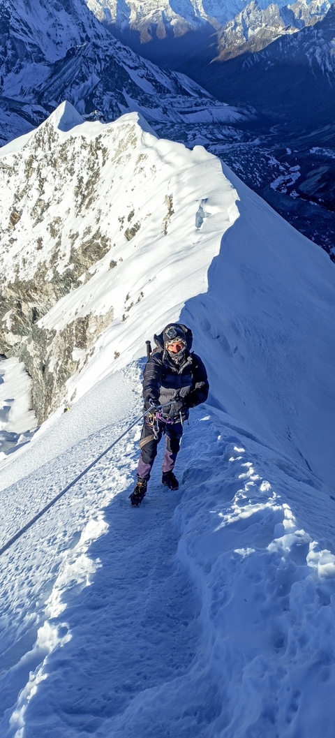 Mountaineer climbing a snowy ridge with safety gear.