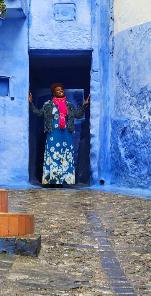 Person standing in a blue alley with a dress and scarf.