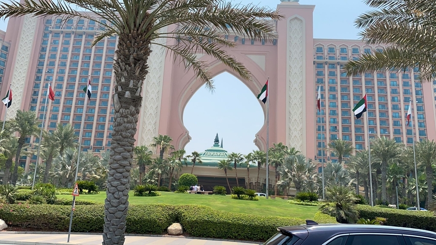 Grand hotel entrance with palm trees and flags.