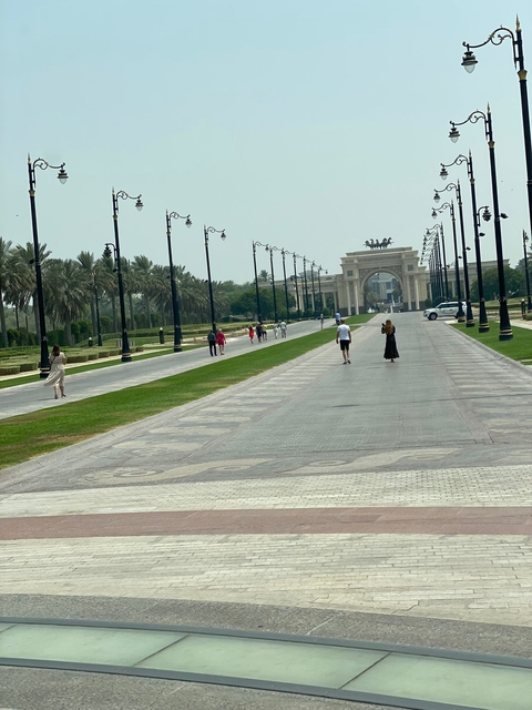 People walking along a wide boulevard with palm trees and an archway.