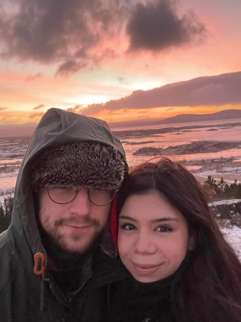 Two people in winter clothing with a snowy landscape at sunset.