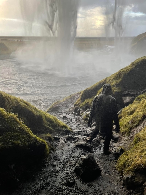 Person walking towards a waterfall through misty rocks.