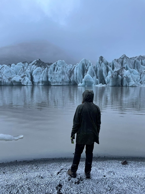 Person in a hooded jacket looking at a glacier over a body of water.