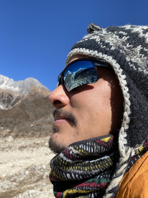       Close-up of a man's face reflecting mountains in sunglasses.
  
