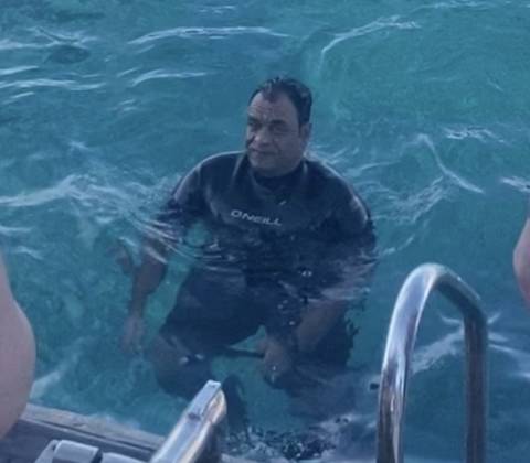       Person in wetsuit sitting in water, partially submerged.
  