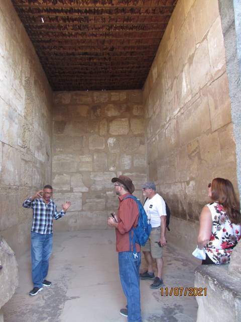      Tourists in an ancient stone room with a guide gesturing.
  