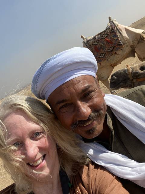       Close-up of two people smiling with a camel in the background.
  