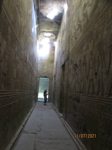 Dimly lit corridor with a person at the end, featuring ancient carvings.