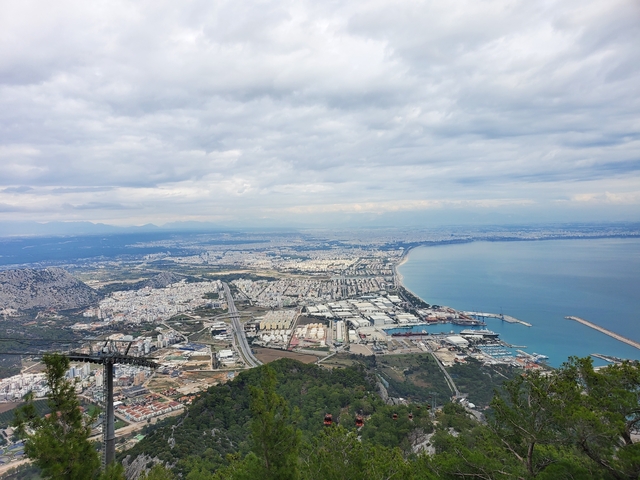      Panoramic view of a coastal city with mountains and a large port.
  