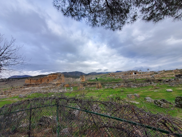       Ancient ruins in a grassy field with rolling hills in the background.
  