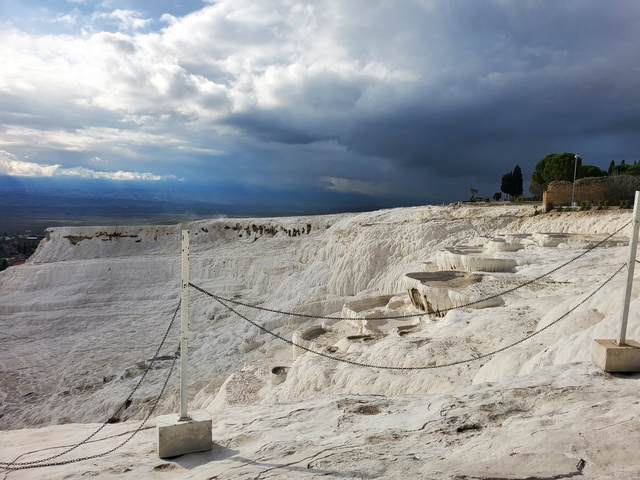       White travertine terraces of Pamukkale under a dramatic sky.
  