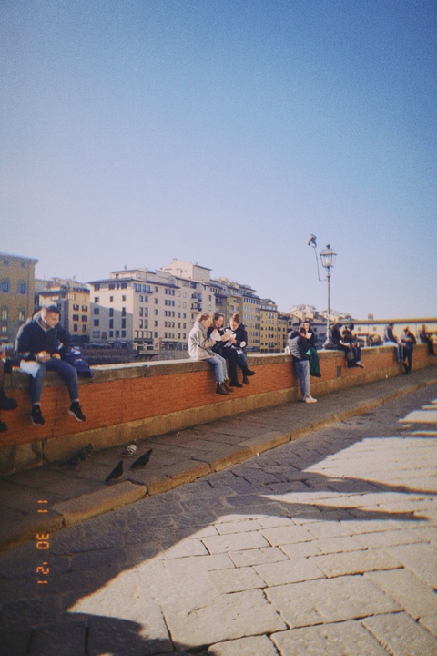       People sitting on a bridge with historic buildings.
  