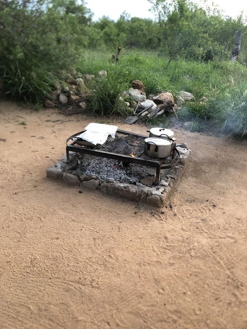 Outdoor cooking setup with pots on a grill over a fire pit.