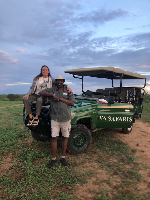       Two people near a safari vehicle in the savannah.
  
