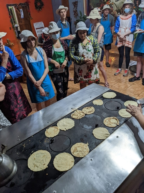      People gathered around a griddle making tortillas.
  