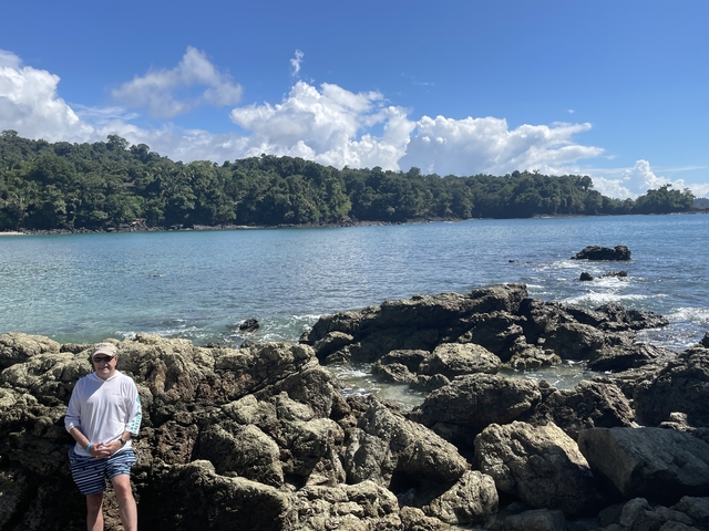       Person standing on a rocky shore with a tropical bay in the background.
  