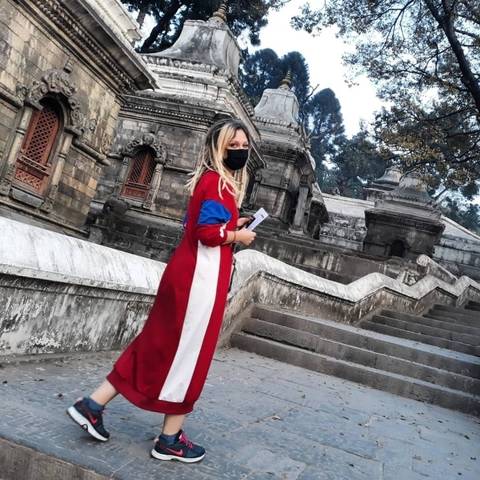       Woman wearing a black mask and red dress in front of a historic temple.
  