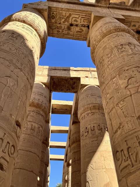       Ancient columns with hieroglyphic carvings and a clear blue sky.
  