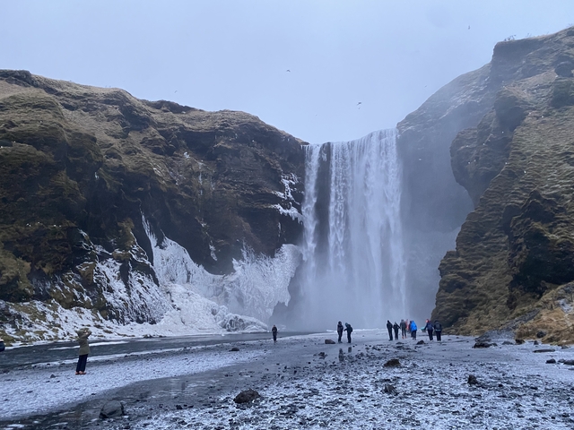 Tall waterfall surrounded by cliffs and people standing below.