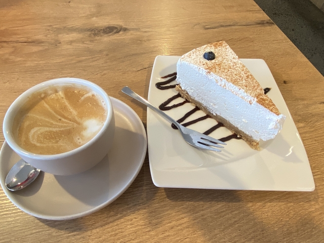 Slice of cake with a cappuccino on a wooden table.