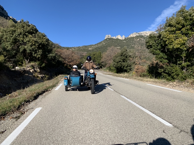 Two people riding a motorcycle with a sidecar on a country road.