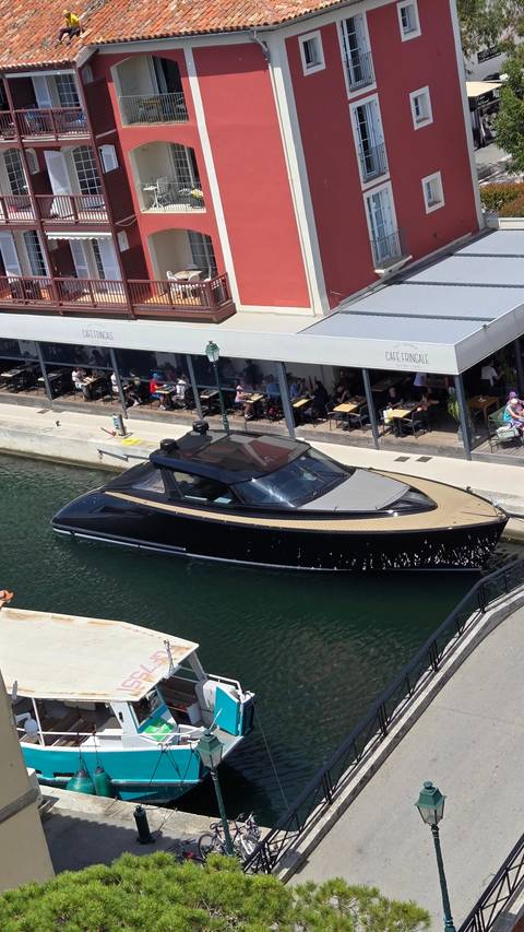 A view of a stylish boat docked alongside a canal with a red building in the background.