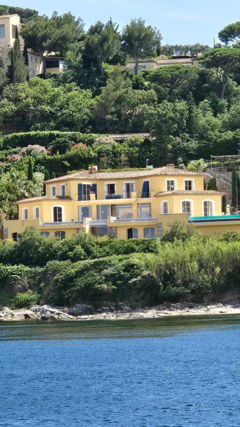 A yellow building surrounded by lush greenery near a waterfront.