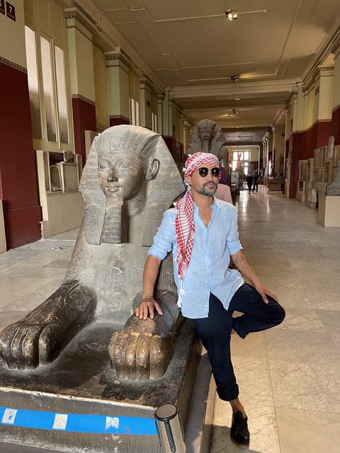Person posing with a sphinx statue indoors.