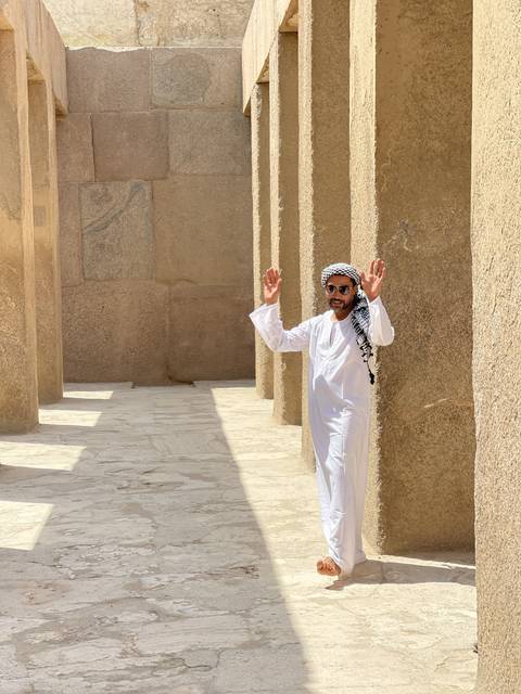 Person in traditional attire waving hands near stone walls.