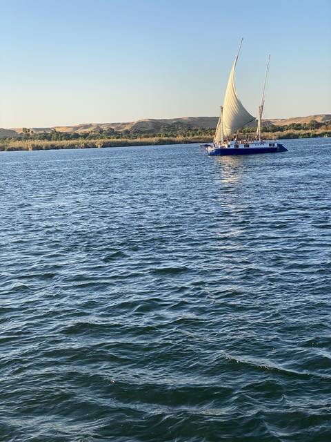       A sailboat on the water with a coastline in the background.
  