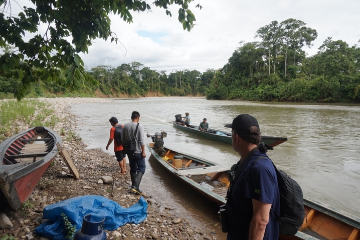Group of people preparing boats on a riverbank.