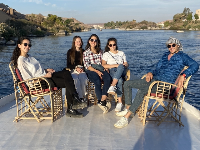 Five people sitting on a boat with a river background.