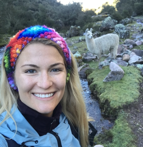       A smiling woman with a llama in a mountainous area.
  