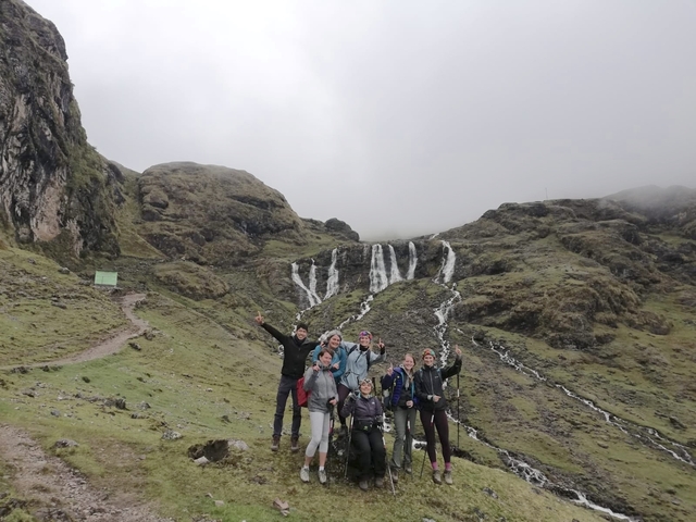       Group of people in front of a waterfall and hills.
  