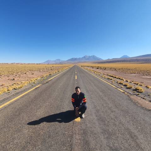 Person kneeling on a long desert road with mountains.
