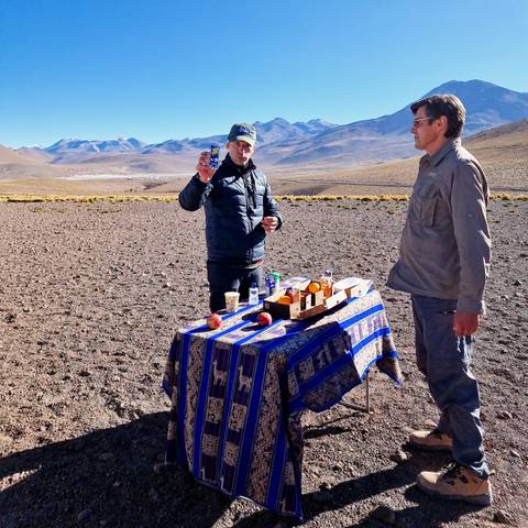 Two people with a table full of snacks in a vast landscape.