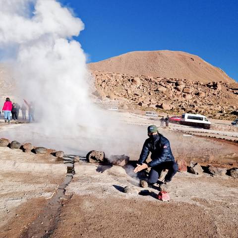 Person posing near a geyser with steam.