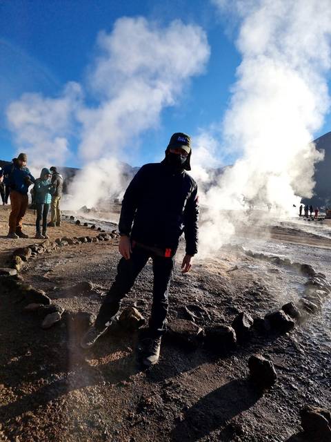 Person standing in a geyser field with steam rising.