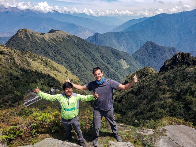       Two people smiling with thumbs up in a mountainous area.
  