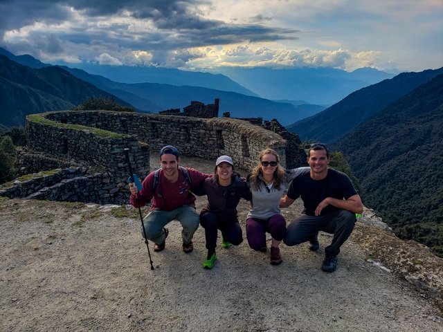       Group of hikers resting at a stone structure with mountain views.
  